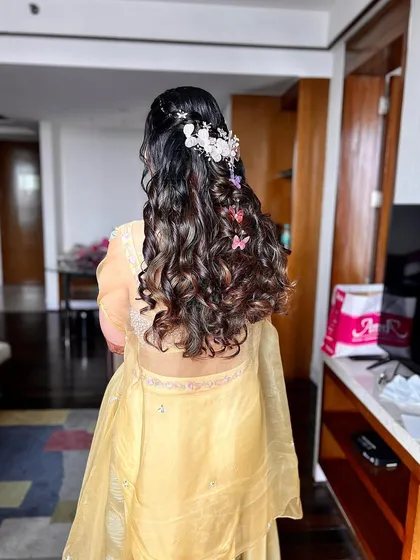 The back view of this intricate haldi hairstyle, combining curls, braids, and beautiful accessories.