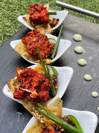 A spicy and flavorful chicken appetizer served on a crispy potato wafer. The contrast of textures and the vibrant red color make this a very appealing dish.