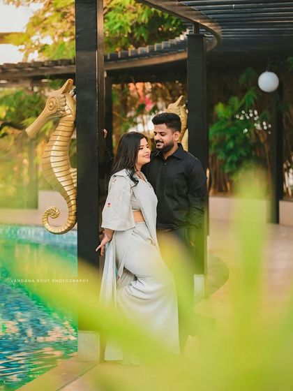 A relaxed and stylish poolside shoot. The lush green surroundings and calm water provide a beautiful, resort-like setting for casual and romantic couple photos.