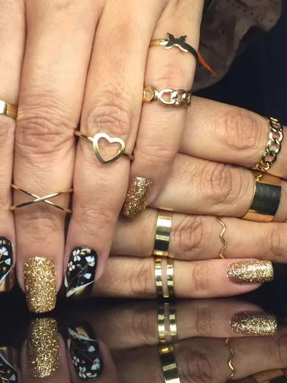 A stunning black and gold manicure featuring floral patterns, gold glitter, and gold chrome accents.