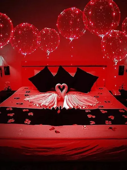 A dramatic and romantic room decoration using red LED balloons. The swan towel art on the bed and scattered petals create a luxurious and intimate atmosphere perfect for a honeymoon or anniversary.