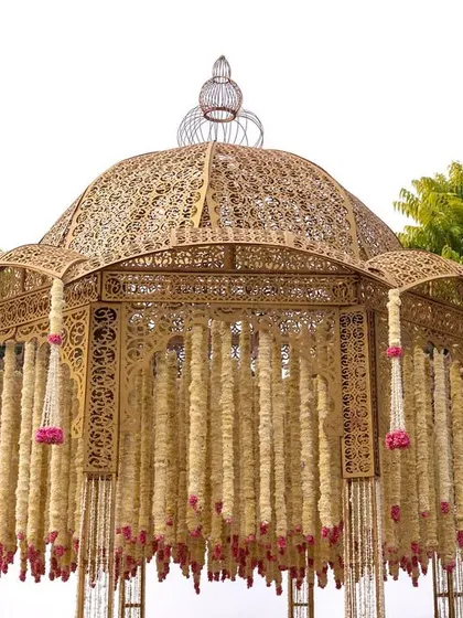 A close-up of the intricately designed golden mandap. The structure is adorned with strings of delicate flowers, adding a touch of softness to the grand design.