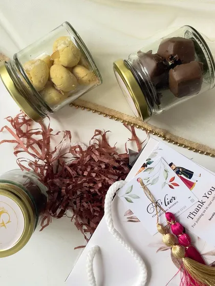 A deconstructed view of our engagement return gift, showing the jars of panned nuts, custom sticker, and personalized thank you card.