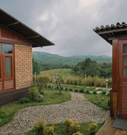 A view between two brick cottages in Sakleshpur, looking out onto the rolling green hills of the Western Ghats.