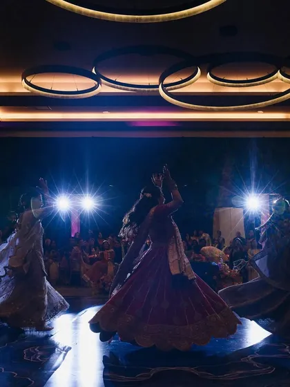 A dramatic shot of the bride and her bridesmaids during their sangeet performance. The backlighting and coordinated outfits create a powerful and visually stunning image.