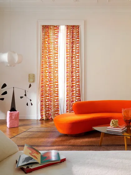 A vibrant living room brought to life by the fearless use of color and form from our Élitis collection. The bold orange curved sofa and graphic curtains create a dynamic interplay, showcasing how our textiles can define a space with energy and modern sophistication.