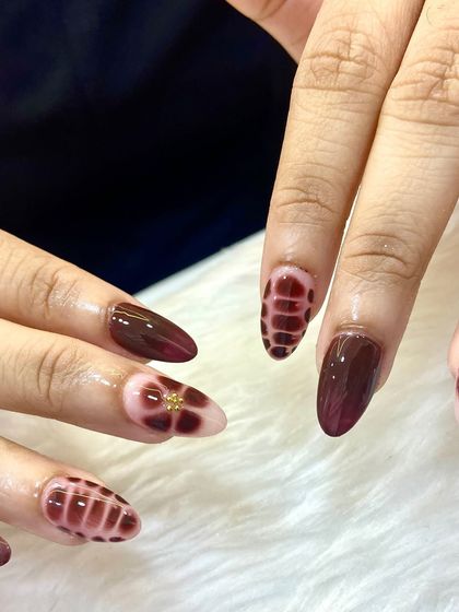 These nails are certified showstoppers. A beautiful and intricate design in deep burgundy, featuring a unique plaid-like texture and floral accents.