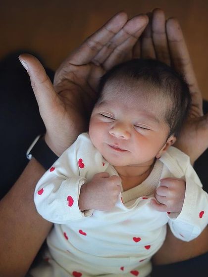 A newborn rests safely in their father's hands. This pose emphasizes how tiny and precious they are, creating a timeless and heartfelt portrait.