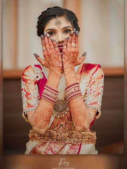 A playful pose showing off the intricate mehndi design. The makeup, with its defined eyes and bold lip, perfectly complements the traditional bridal details.