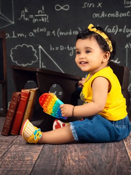 A baby girl sits in a "Class of 2022" setup, complete with a chalkboard, books, and a globe. A fun way to imagine their bright future.