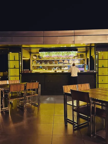 A view of the rooftop bar during service. The back-lit shelving and overhead lighting fixture, which also serves as a planter, create a functional and atmospheric centerpiece for the cafe.
