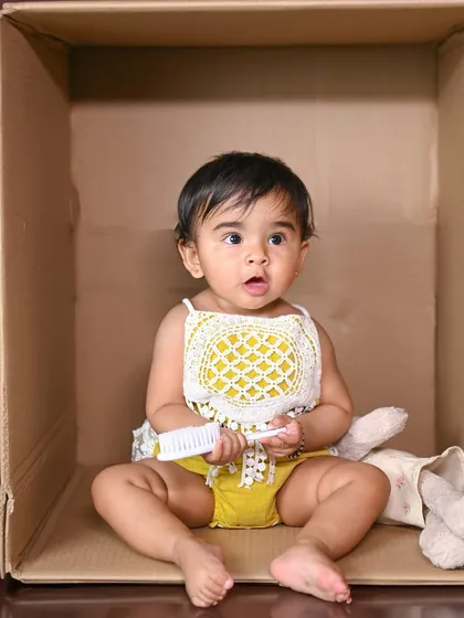 A curious baby peeking out of a cardboard box, holding a little toy.