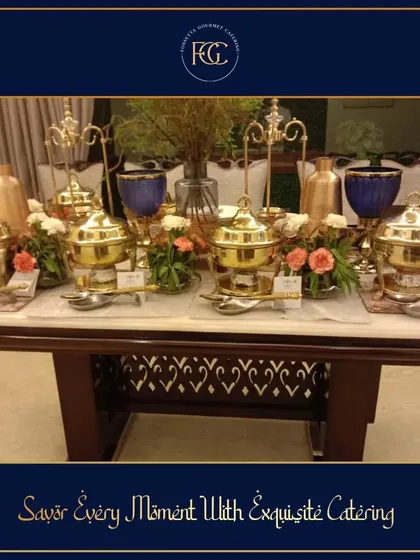 Savor every moment with exquisite catering. A beautifully set buffet on a marble-top table, featuring our signature brass serving dishes and elegant floral arrangements for an intimate gathering.