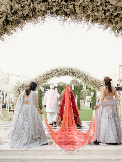 The bride's dramatic entry, with her bridesmaids holding her long, beautiful veil, framed by an arch of white flowers.