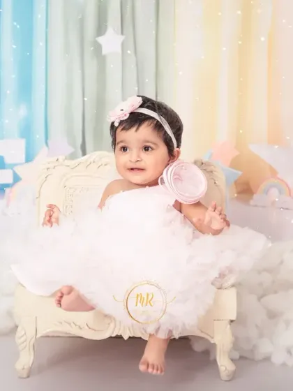 A princess moment for this one-year-old, sitting on a miniature throne in her pastel rainbow and cloud-themed birthday set.