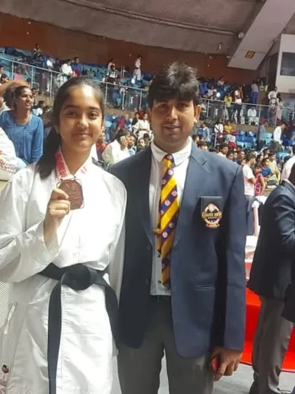 A black belt student with her medal at the Talkatora Indoor Stadium, showing her experience at a high-stakes international event.
