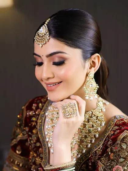 A close-up portrait showcasing the soft, smokey eye makeup and perfectly defined features on this bride in her maroon velvet lehenga.