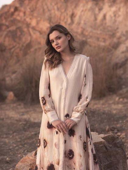 A full-length portrait showcasing a long-sleeved dress with delicate sleeve and placket details. The calm pose and soft lighting are perfect for a brand that values understated elegance.