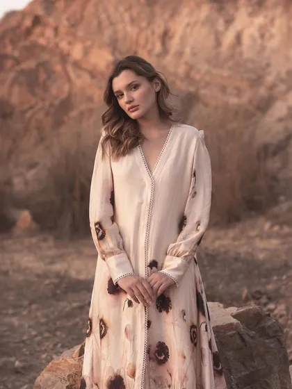 A full-length portrait showcasing a long-sleeved dress with delicate sleeve and placket details. The calm pose and soft lighting are perfect for a brand that values understated elegance.