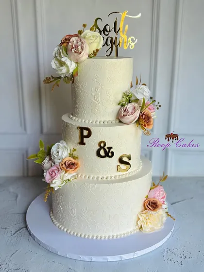 This elegant three-tier cake was designed for a beautiful beginning. It features a subtle floral stencil pattern, soft pastel blooms, and the couple's initials in gold for a personalized touch.