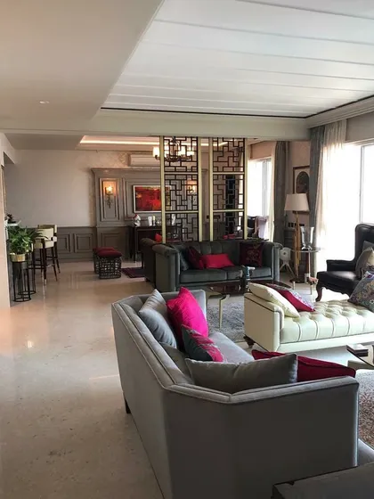 This living space is designed as an amalgamation of styles, blending classic comfort with contemporary details. The open-plan layout is defined by a geometric screen partition, creating distinct zones for lounging and a home bar while maintaining a cohesive flow.