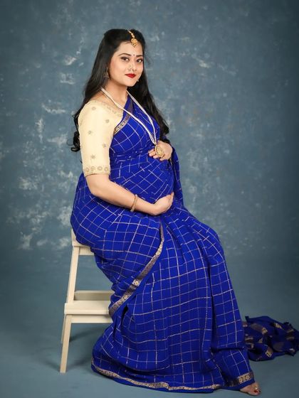 A full-length portrait of a beautiful mom-to-be seated in a traditional blue saree. This classic pose is perfect for showcasing both the baby bump and the elegance of the ethnic attire.