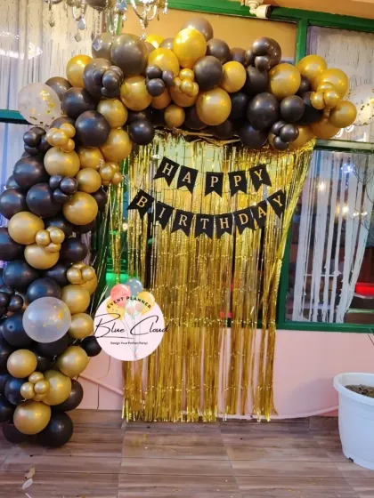A black and gold balloon arch with a gold shimmer curtain, perfect for an elegant at-home party.