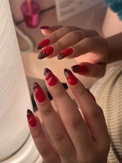 The light catches the glossy finish of these dramatic red and black nails, highlighting the intricate, hand-painted patterns.