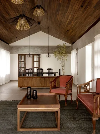 The living and dining area of the Polibetta Farmhouse features a repurposed wooden false ceiling, adding warmth and history to the space. We combine minimalist cement finishes with classic furniture to create a balanced, pared-back aesthetic.