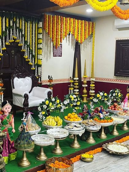 A beautiful setup for a baby shower or naming ceremony. The decor includes a traditional 'jhoola' (swing) chair, marigold garlands, and a table laden with fruits and sweets, creating a festive and welcoming atmosphere.