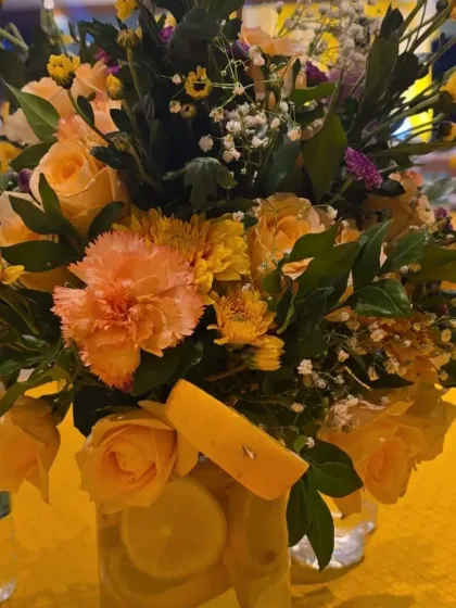 A beautiful floral centerpiece for the Haldi, featuring yellow roses and carnations with slices of lemon in the vase for a fresh, unique touch.