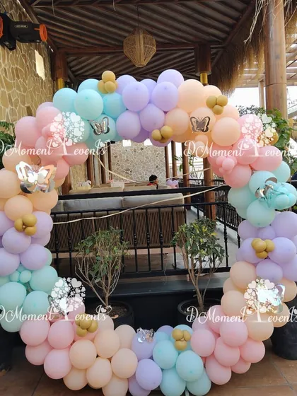 A circular balloon frame in pastel colors, perfect for a photo booth. The arch is decorated with silver butterfly stickers, adding a touch of sparkle.
