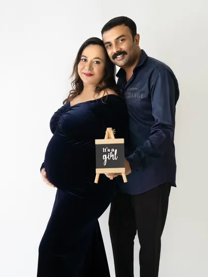A perfect gender reveal photo, with the couple holding a small sign that says "It's a girl" while smiling at the camera.