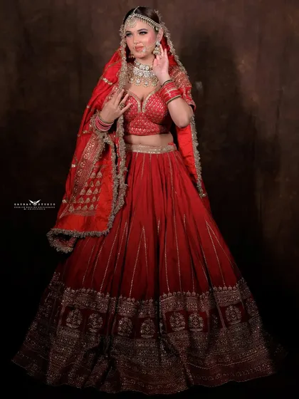 A full-length shot of the bride in her red lehenga against a dark, classic studio backdrop.