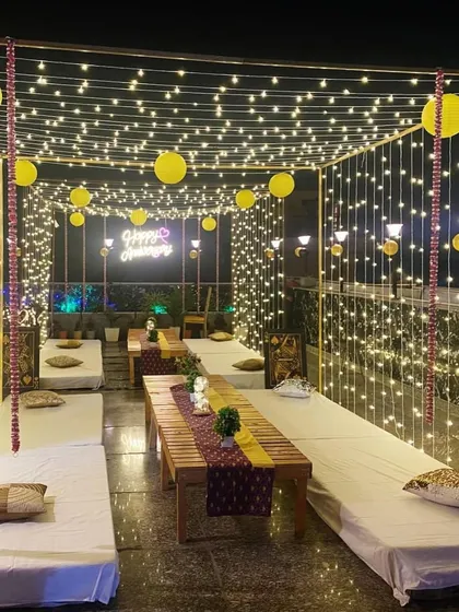 An elegant terrace arrangement for an anniversary, featuring long tables with low seating and a canopy of lights with yellow paper lanterns.