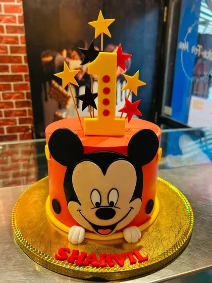 A vibrant Mickey Mouse cake for a first birthday celebration. The design features Mickey's iconic face, topped with a number '1' and stars for a magical touch.