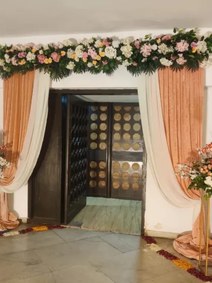 A sophisticated doorway decoration with a floral header made of pastel roses and elegant peach-colored drapes. This design adds a touch of class to any home entrance.