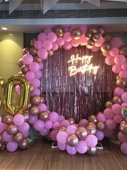 A glamorous 60th birthday decoration in pink and rose gold. The circular balloon arch is set against a shimmering backdrop with large gold foil numbers.