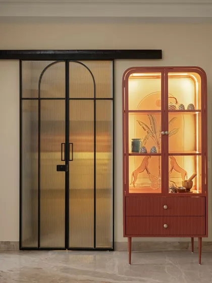 A striking red-orange cabinet with fluted glass doors stands next to the entrance of the dining room, adding a bold pop of color and functional storage.