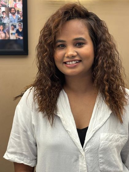 A smiling client with her newly colored and styled curly hair. The look is fun, vibrant, and full of personality.