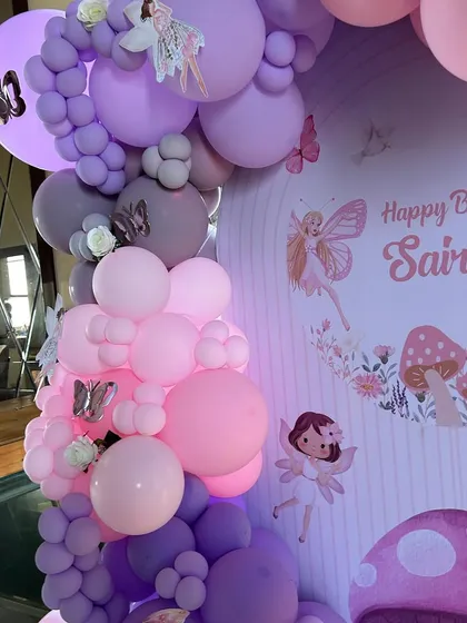 A side view of the fairy-themed balloon arch, showing the depth and dimension of the arrangement. The combination of different balloon sizes and colors, along with fairy and butterfly accents, creates a rich, textured look.