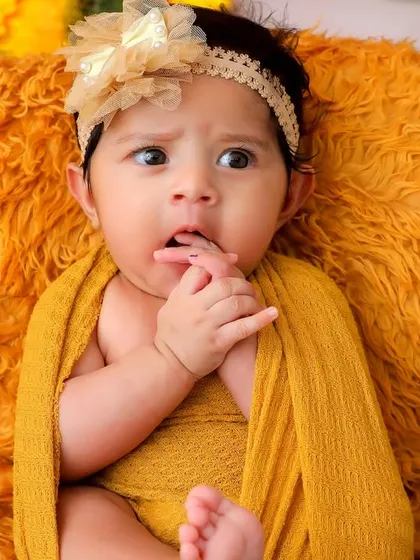 A curious glance from a newborn baby nestled in a basket surrounded by sunflowers. The warm colors and soft textures create a cozy and inviting scene.
