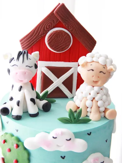 The top of the farm cake, featuring a cute cow and a fluffy sheep sitting by the red barn, all made from fondant.