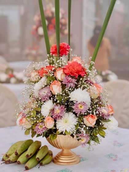 A beautiful table centerpiece in a brass bowl, with a bunch of green bananas placed alongside as a traditional and symbolic touch.