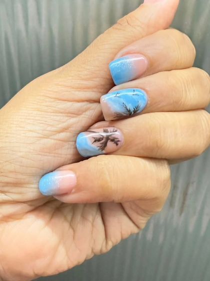 A beach-themed manicure with a blue ombre base and hand-painted palm tree silhouettes for a perfect vacation vibe.