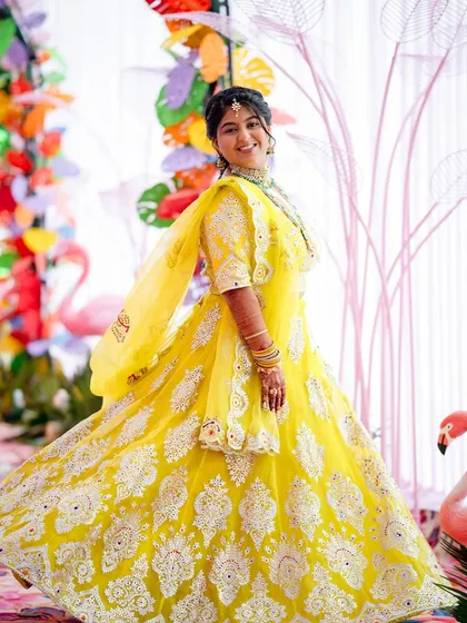 A close-up of a bride in her vibrant yellow lehenga, perfectly matching the colourful, flamingo-themed decor of her Mehendi event.