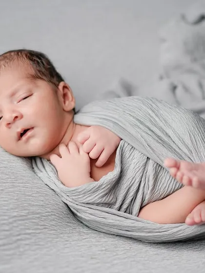 Drifting off to sleep. This image captures that in-between moment of a newborn settling, with his tiny hands held close, wrapped in a soft grey swaddle.