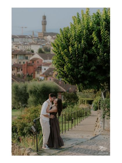 A romantic kiss in a garden overlooking the historic city of Florence, Italy. The cityscape in the background provides a stunning context for this intimate pre-wedding moment.