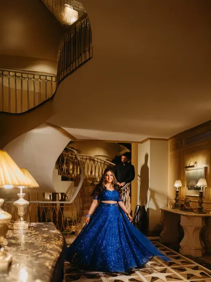 A grand, sweeping shot of Raakhee on the staircase in her dazzling blue lehenga, with Akshay in the background. A true fairytale moment.