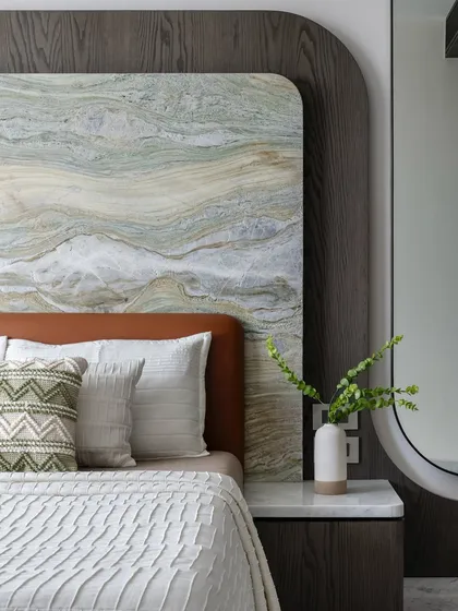 A close-up of the bed in 'The House of Arcs', showing the textural play between the stone headboard, leather base, and soft linen.